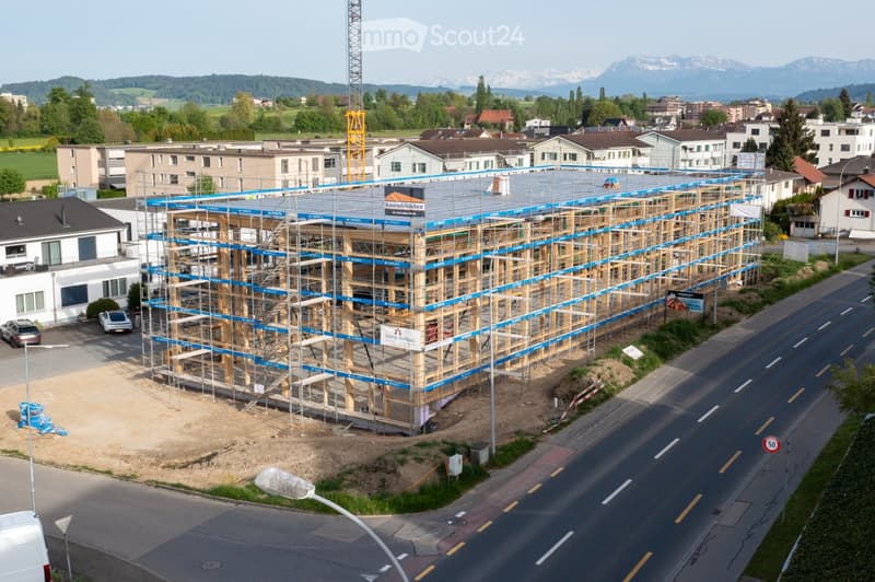A multi-story building under construction with scaffolding, surrounded by other residential buildings and a road.