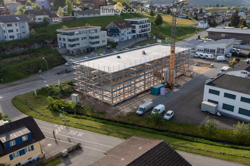 Aerial view of a construction site with a building under construction, surrounded by residential houses, vans, and a crane.