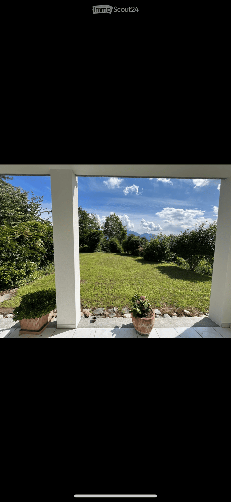 A spacious garden with a well-maintained lawn, surrounded by trees and shrubs, visible through a large open doorway.