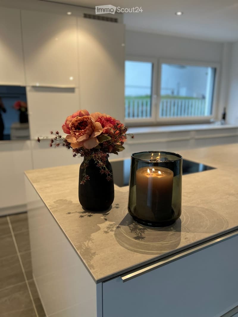 Modern kitchen with white cabinets, a light-colored countertop, and a vase with flowers and a lit candle on the counter.
