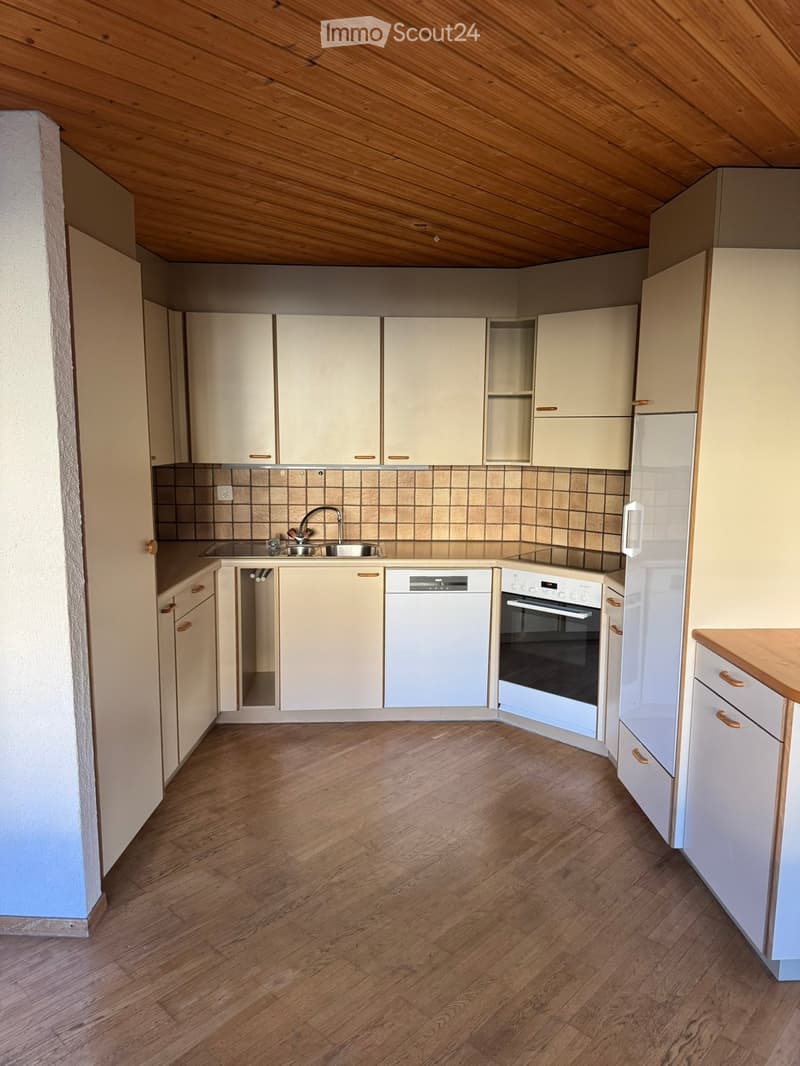 Modern kitchen with light-colored cabinets, wooden flooring, and stainless steel appliances including a sink, dishwasher, and oven.