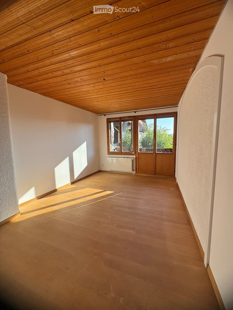 Empty room with wooden floor, white walls, large windows, and a radiator. No furniture or equipment present.