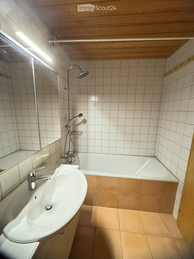 Modern bathroom with a white sink, bathtub, and showerhead. The walls are tiled, and the floor is tiled with beige tiles.