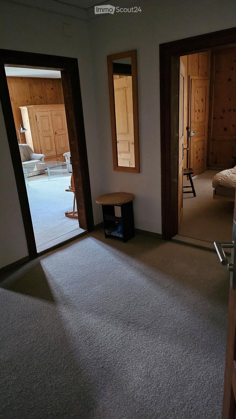 Carpeted hallway with open doors leading to a living room and bedroom, featuring a small round table and a mirror on the wall.