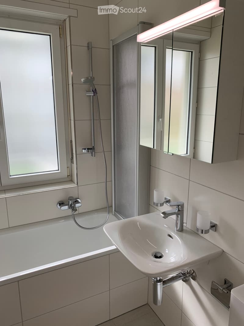 Modern bathroom with a bathtub, sink, chrome faucet, mirror cabinet, and candles on the sink counter.