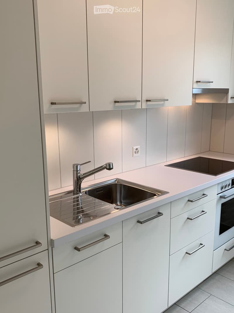 Modern kitchen with white cabinets, stainless steel sink, faucet, and oven. Light-colored countertops and sleek design.