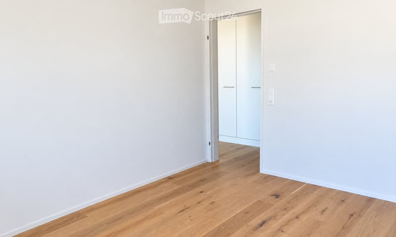 Empty room with light-colored walls and wooden flooring, featuring a doorway leading to another room with built-in wardrobes.
