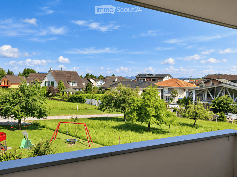 View from a balcony overlooking a residential area with houses, trees, and a playground in the foreground.
