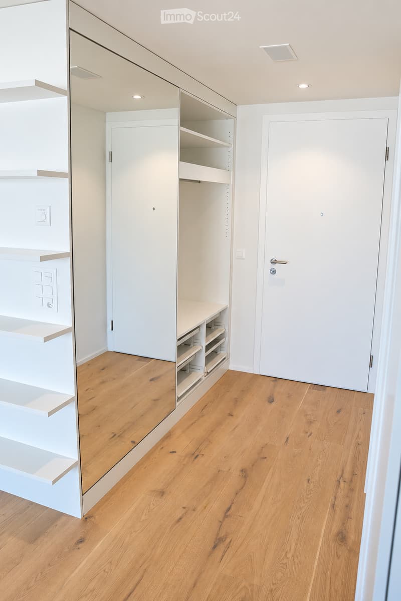 Empty room with light wooden flooring, white walls, built-in closet with shelves and drawers, and a closed white door.