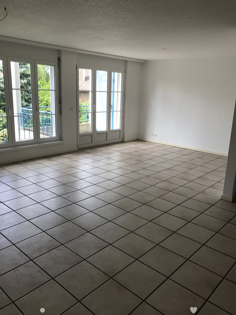 Empty room with tiled floor and large windows, including a sliding glass door leading to a balcony.