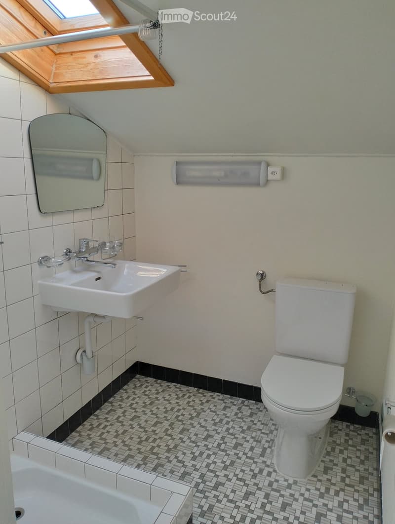 Modern bathroom with white tiles, a white sink, a toilet, a bathtub, and a large mirror above the sink. The floor features a black and white patterned tile design.
