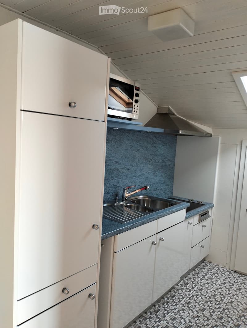 Modern kitchen with white cabinets, stainless steel sink, microwave, and grey countertop.