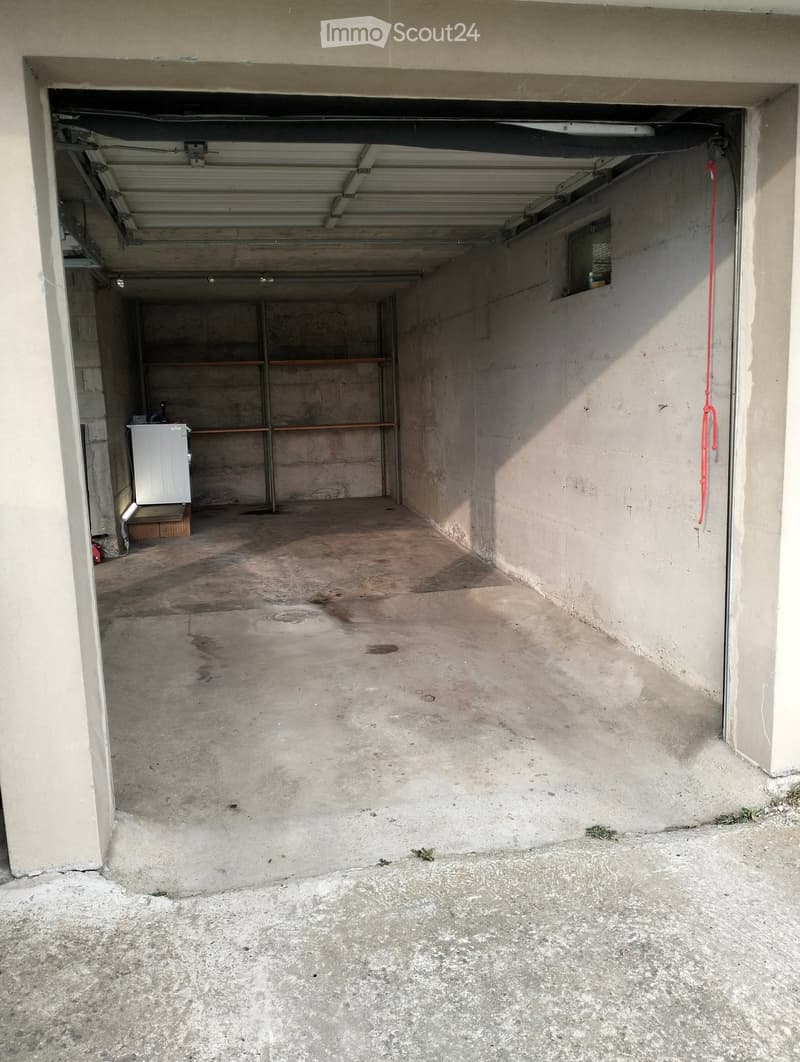 Empty garage with concrete floor, metal shelving unit, and a small window on the right wall.
