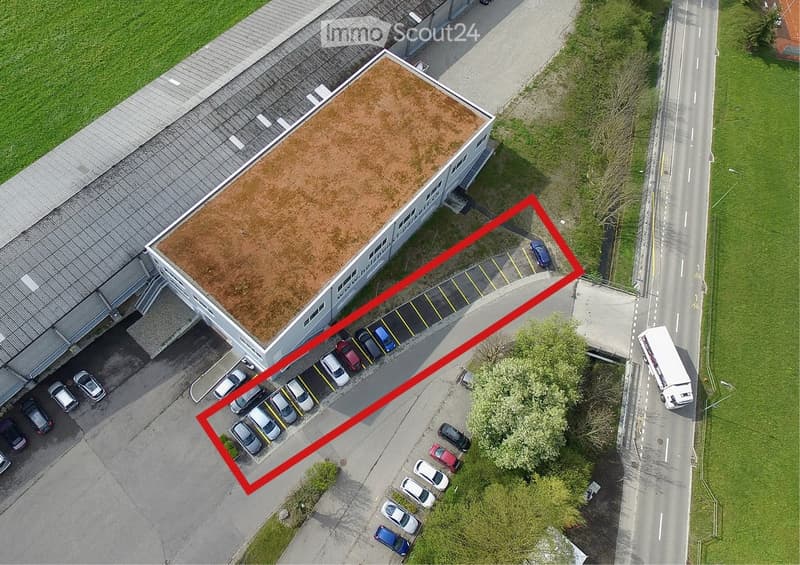 Aerial view of a commercial building with a flat roof and a parking lot with multiple cars.