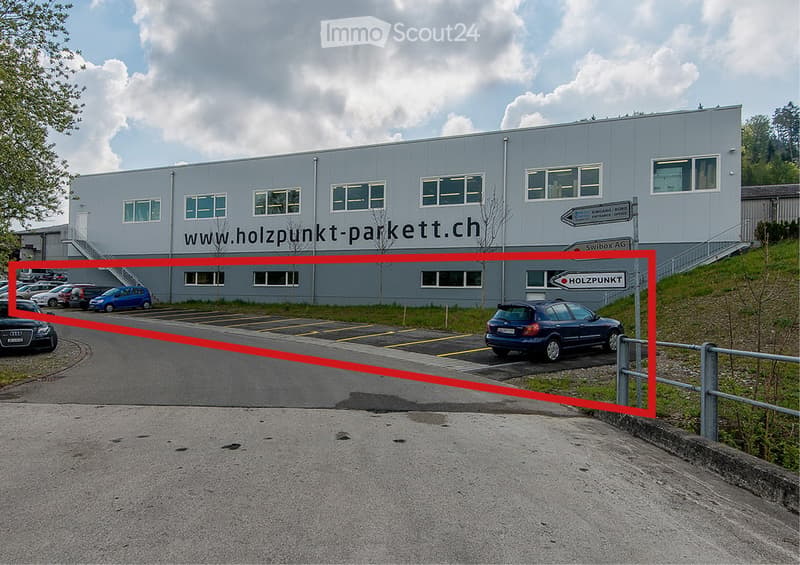 Modern industrial building with large windows and signage for "www.holzpunkt-parkett.ch" and "HOLZPUNKT".