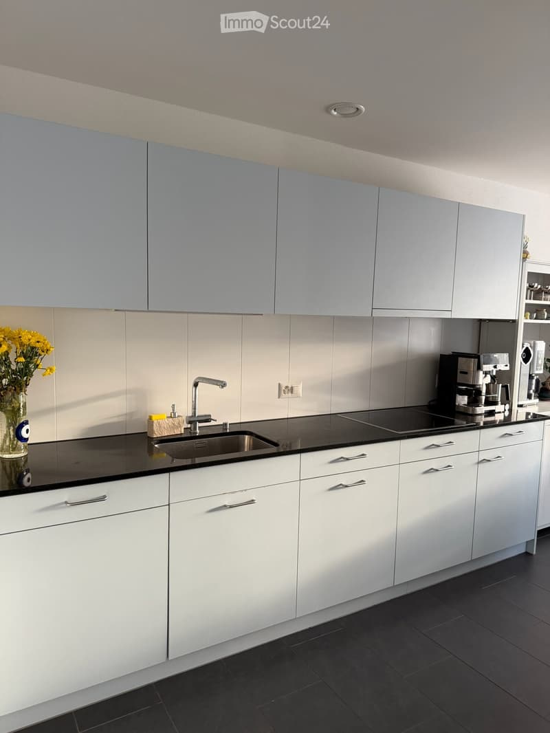 Modern kitchen with white cabinets, black countertops, stainless steel sink, and a coffee machine on the counter.