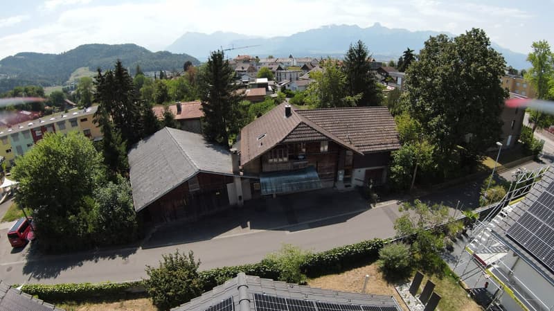 Aerial view of a residential area with multiple houses, surrounded by trees and mountains in the background.