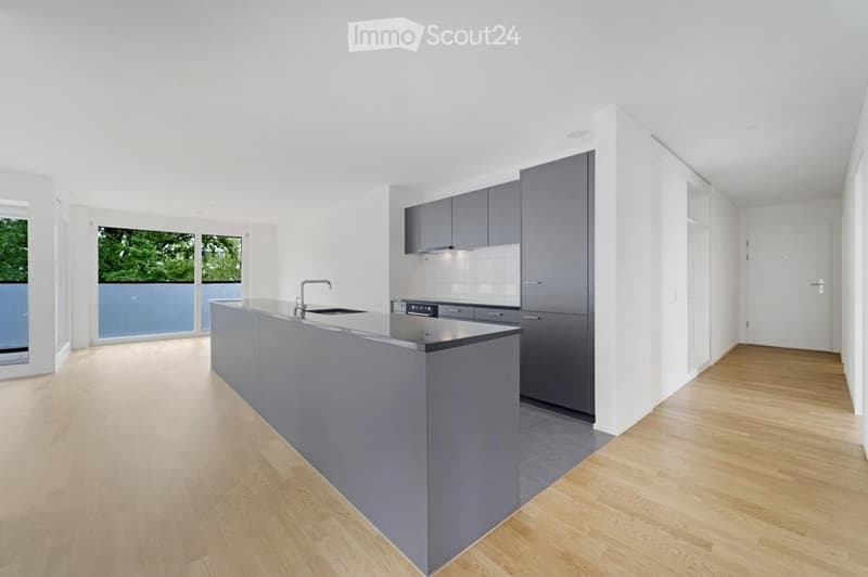 Modern kitchen with grey cabinets, a central island, and a sleek faucet. Large windows provide natural light, and the floor is light wood.