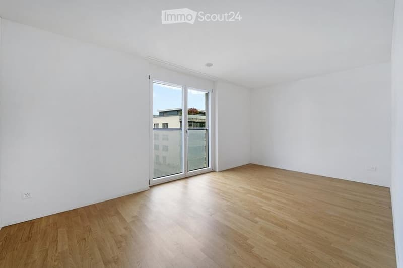 Empty room with white walls, wooden flooring, and large glass sliding doors leading to a balcony.