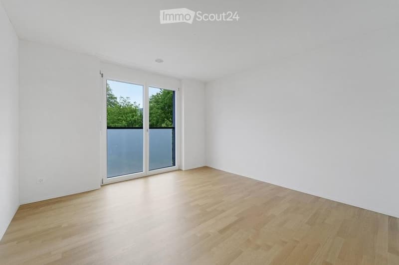 Empty room with white walls, wooden floor, and large sliding glass doors leading to a balcony.