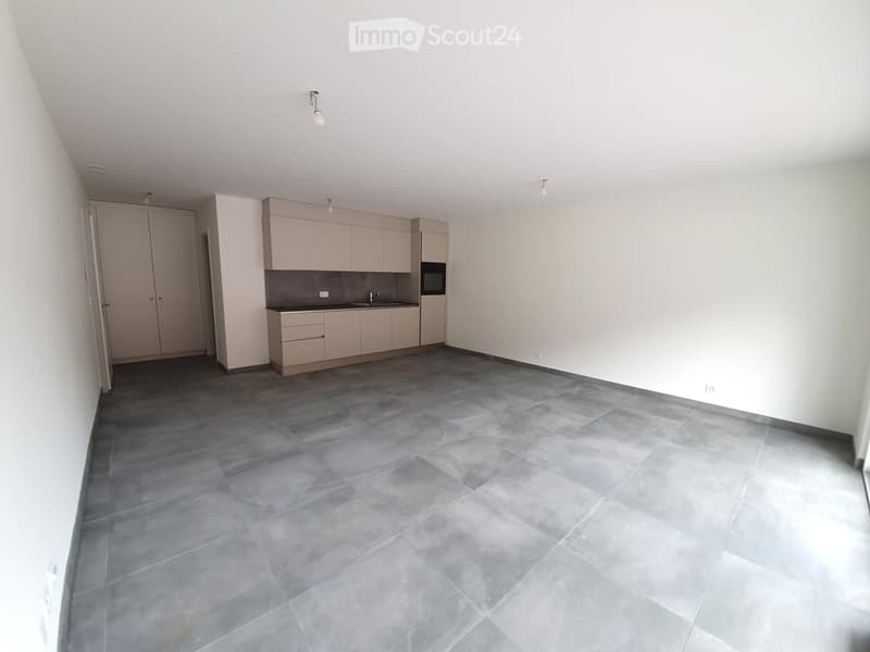 Empty kitchen with light-colored cabinets, a sink, and a built-in oven. The floor is covered with large, dark gray tiles.