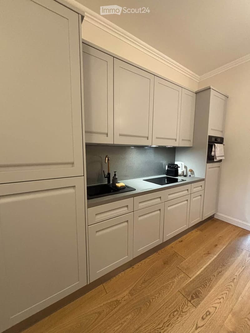 Modern kitchen with light-colored cabinets, a sink, a faucet, an oven, and a microwave. The countertops are clean and the floor is made of light wood.