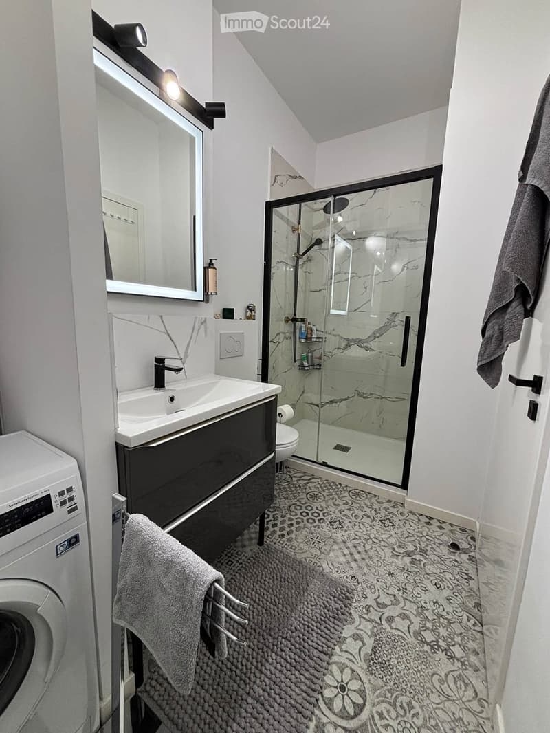 Modern bathroom with a white sink, black vanity, large mirror, glass-enclosed shower, and decorative tile floor.