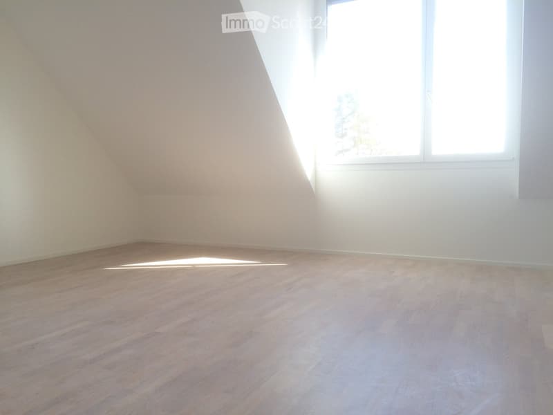 Empty room with wooden flooring and white walls, featuring a large window allowing natural light to enter.