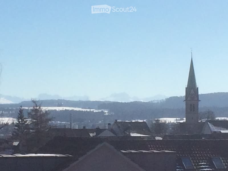 A town view with a prominent church tower and surrounding rooftops, snow-covered landscape in the background.