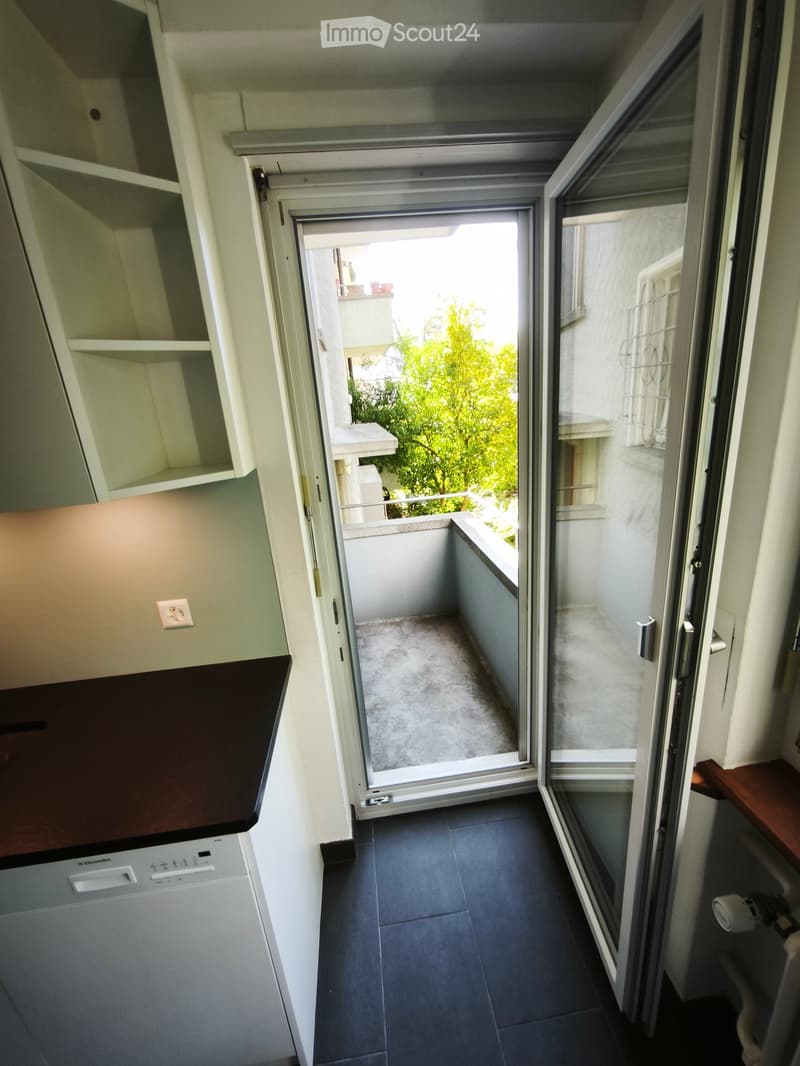Balcony with sliding glass doors, view of greenery, small concrete floor, white walls, and railing.