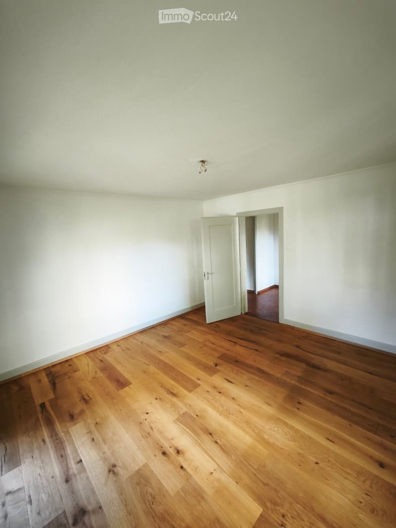 Empty room with light-colored walls and wooden flooring, featuring a single white door leading to another room.