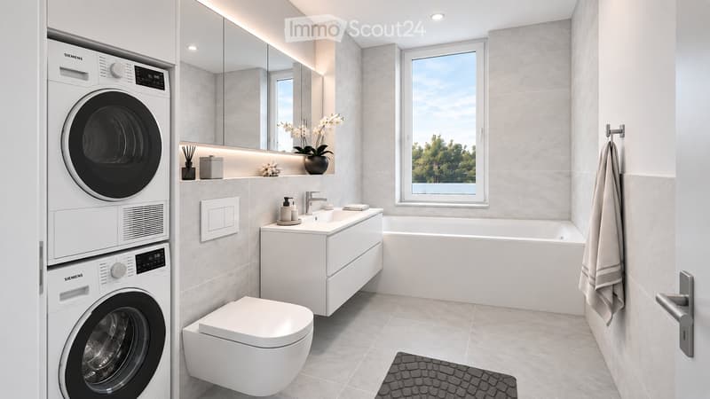 Modern bathroom with a white washing machine and dryer, toilet, sink, bathtub, large mirror, and a window with a view of greenery.