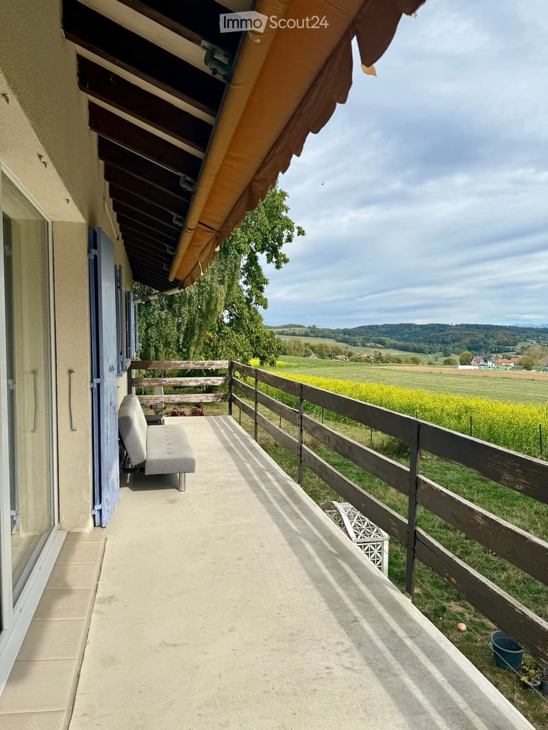 Balcony with wooden railing, grey bench, and scenic countryside view.