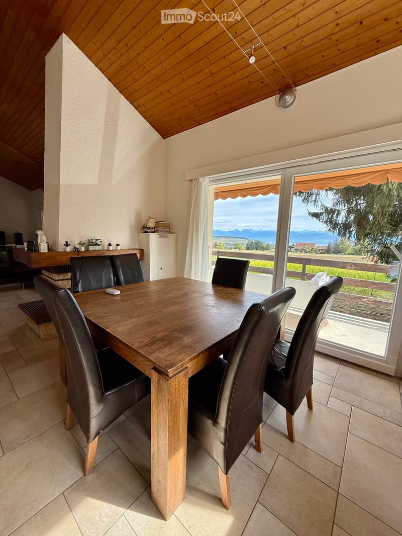 Dining room with a wooden dining table, six black leather chairs, a cabinet, and a large window offering a scenic view of mountains and greenery.