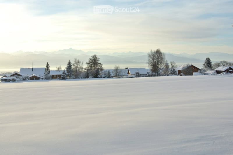 A serene snowy landscape with scattered houses, trees, and distant mountains under a clear sky.