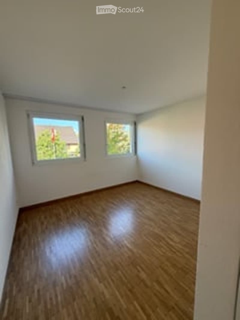 Completely empty room with wooden flooring and white walls, featuring two windows with natural light.