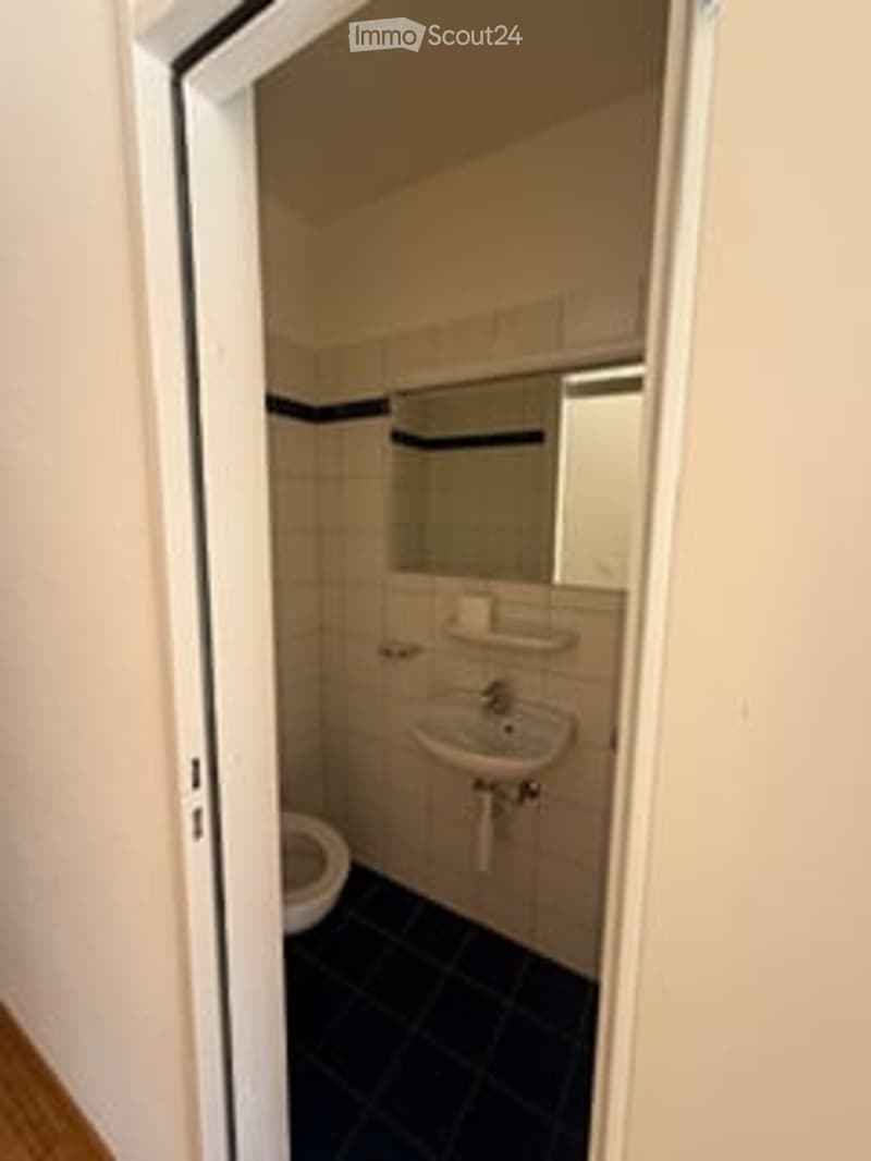Small bathroom with white tiled walls, black tiled floor, toilet, sink, and mirror.