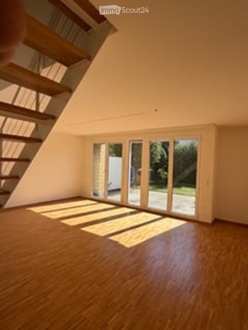 Bright, empty room with wooden flooring, large glass sliding doors leading to a balcony, and natural light streaming in.