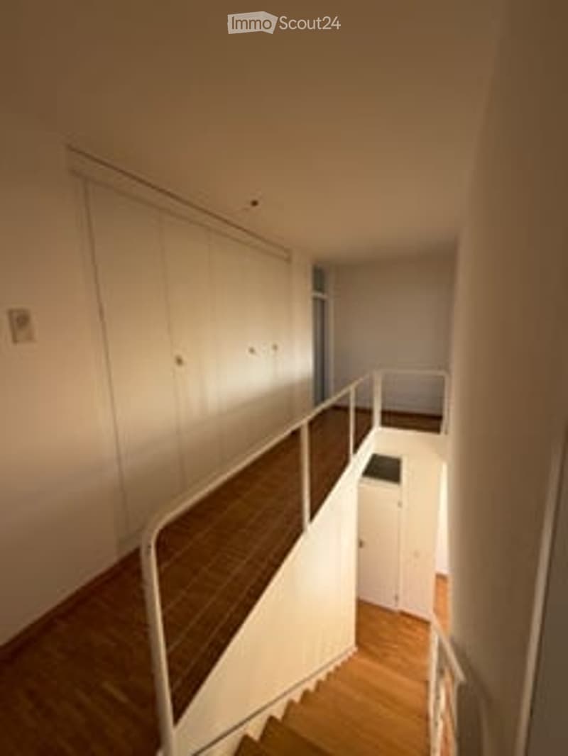 Empty staircase leading to an upper level, with wooden steps and a white railing, adjacent to a small white closet area.