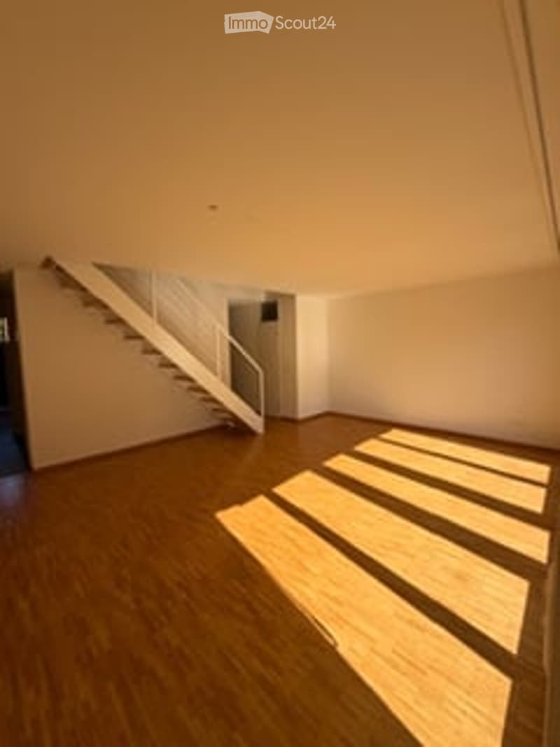 Empty room with wooden flooring and white walls, featuring a staircase leading upwards.