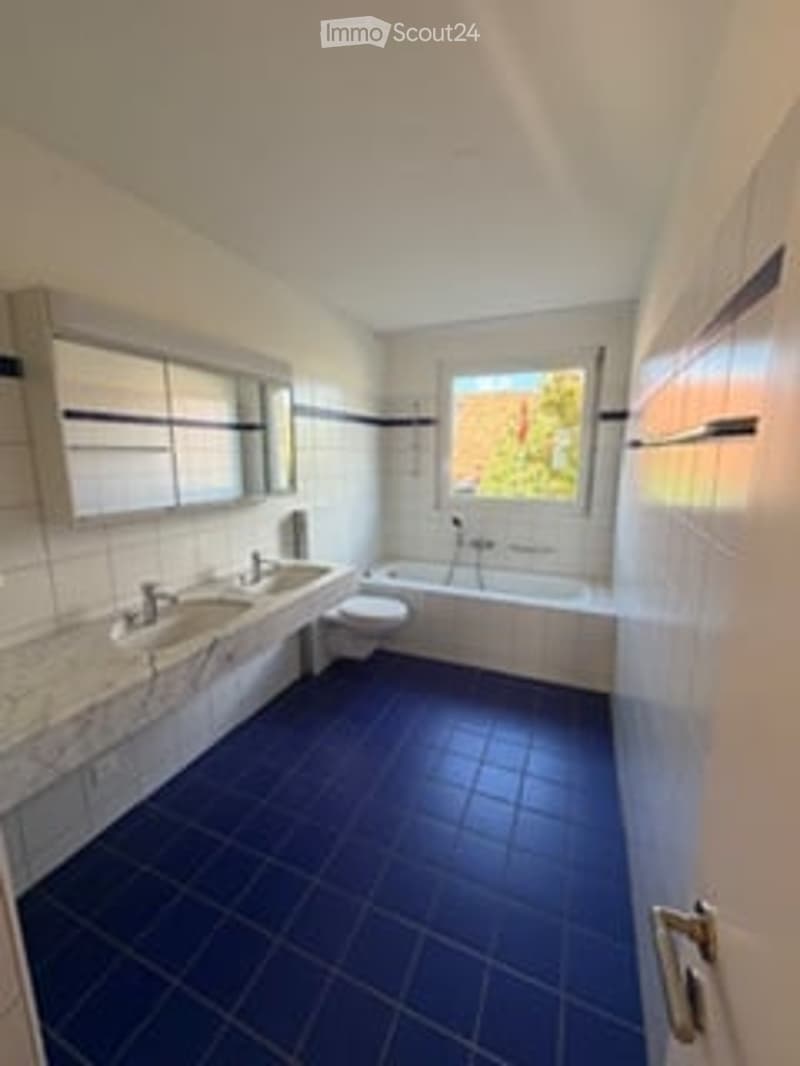 Modern bathroom with blue tiled floor, marble countertop, double sink, bathtub, and large window.