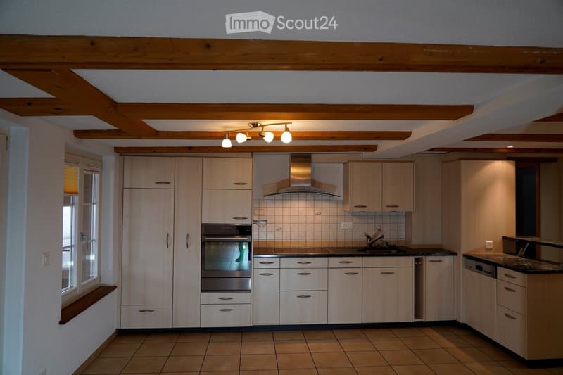 Modern kitchen with wooden cabinets, stainless steel appliances, tiled floor, wooden beams, and under-cabinet lighting.
