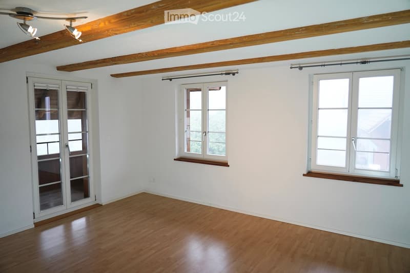 Spacious room with wooden floor, white walls, three windows, and wooden beams in the ceiling