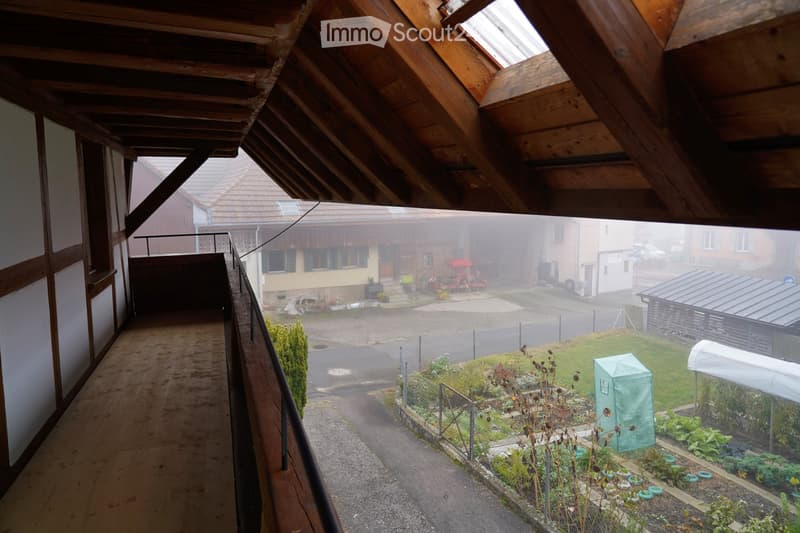 Balcony of a house, wooden structure, surrounded by a garden and road
