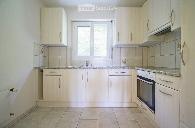 Bright kitchen with light wooden cabinets, granite countertops, and a built-in oven. Features a window above the sink and tiled backsplash.