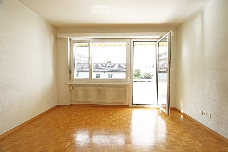 Empty room with wooden flooring, white walls, large window with blinds, and a radiator below it. No furniture or equipment present.
