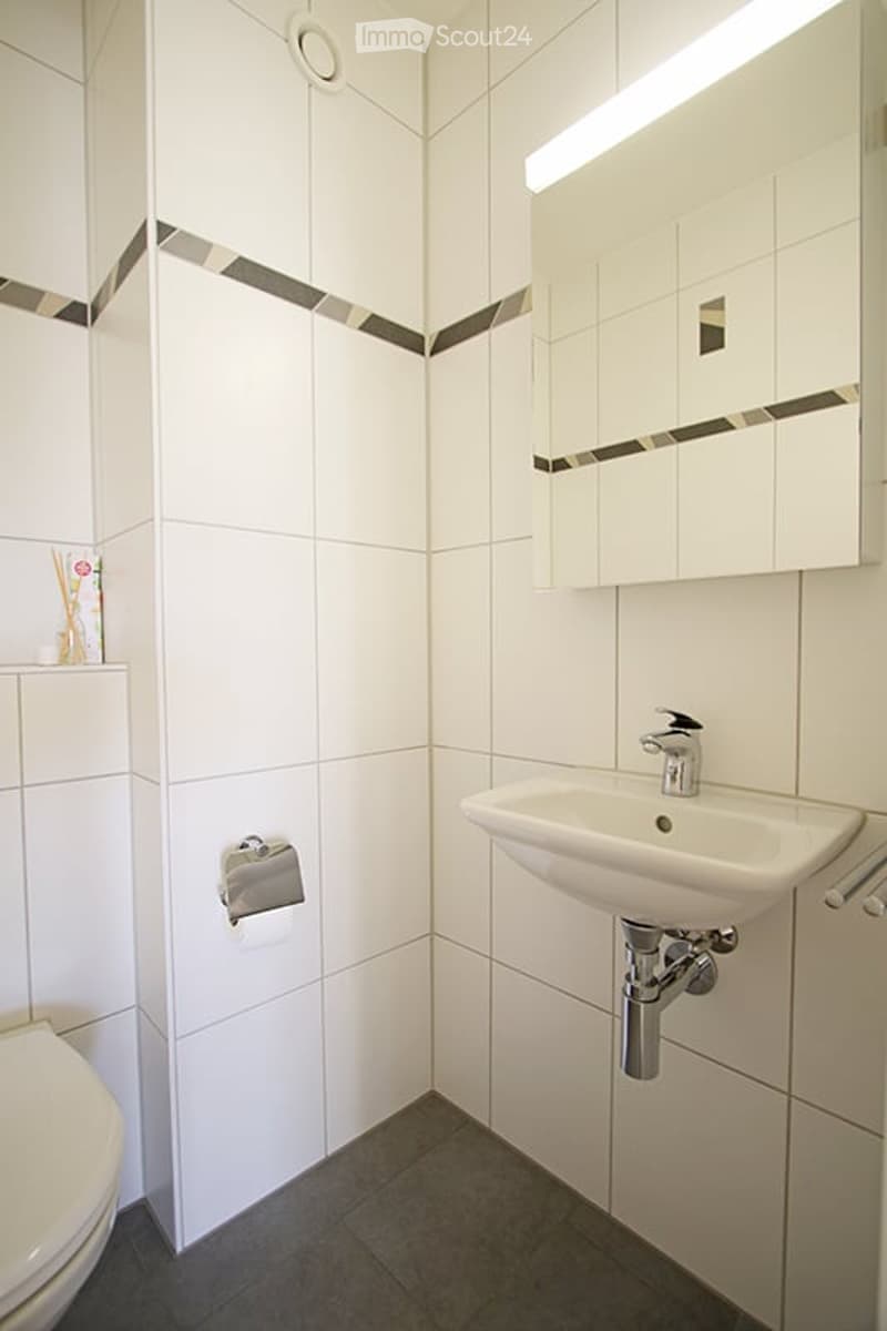 Modern bathroom with white tiled walls, a white sink, a toilet, and a large mirror above the sink. The walls feature a decorative black and grey border design.