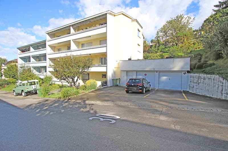 Multi-story residential building with balconies, garage, and parking area.
