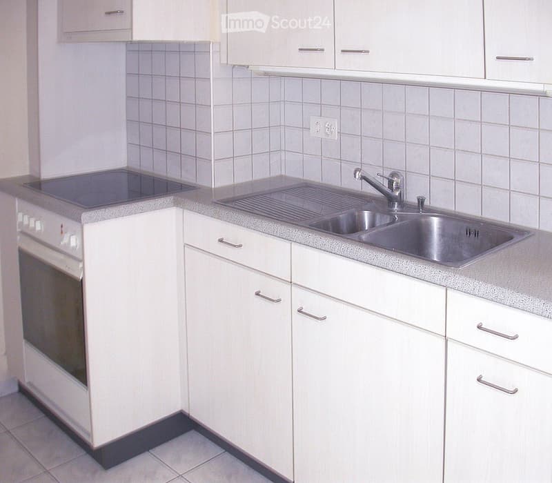 Modern kitchen with white cabinets, a stainless steel sink, and an oven. The countertops are tiled, and the backsplash is also tiled.