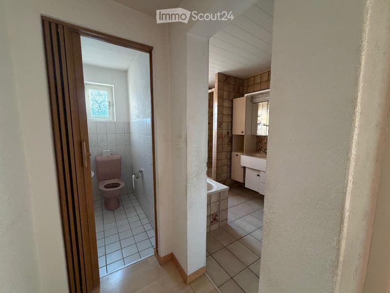 Two adjacent bathrooms with tiled floors and walls, one with a toilet and the other with a sink, bathtub, and cabinet.